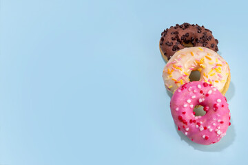 Sweet colorful sugar glazed donuts on light blue background. Three tasty doughnuts - chocolate, vanilla, strawberry pink, copy space