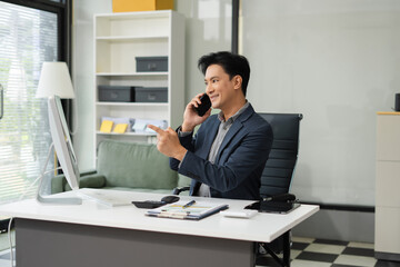 Fototapeta premium Asian Businessman sitting in office using a cellphone and laptop.