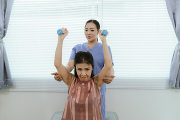 Senior woman exercising with dumbbells during physical therapy in hospital. Physiotherapist helps...