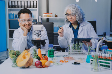Team Asian scientists in a lab conducting food research using a microscope and lab equipment,...