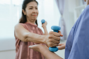Senior woman exercising with dumbbells during physical therapy in hospital. Physiotherapist helps...