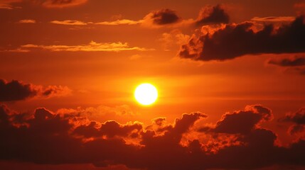 A stunning sunset casts a warm glow over the horizon as the sun dips below the clouds. Vibrant orange and red hues fill the sky, creating a serene atmosphere by the water