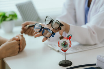 Asian female doctor talking to elderly patient, showing eye model and explaining about eye disease...