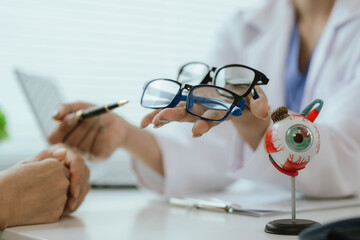 Asian female doctor talking to elderly patient, showing eye model and explaining about eye disease...