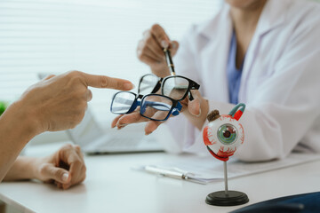 Asian female doctor talking to elderly patient, showing eye model and explaining about eye disease...