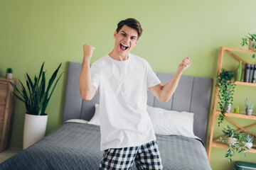 Energetic young man celebrating indoors in sleepwear in a cozy modern bedroom