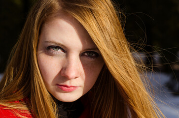 Young woman with red hair stares intensely, half in shadow, bright winter sun illuminating face....