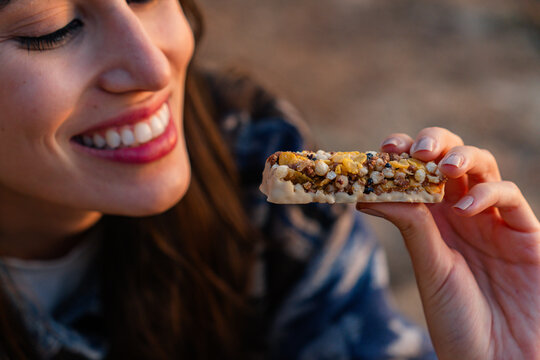 Happy woman enjoying a delicious cereal bar, savoring a healthy snack full of natural grains and seeds during a refreshing break outdoors