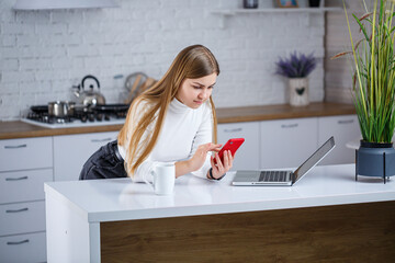 In a modern kitchen, a woman uses her smartphone in a tranquil space with minimalist decor and greenery, creating an ideal environment for multitasking and relaxation during her morning routine
