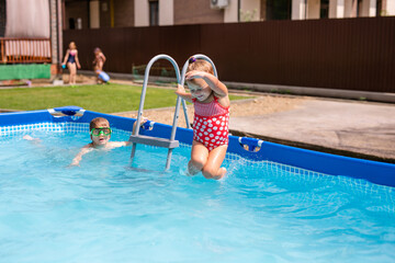 Happy little girl in red swimsuit jumping into outdoor swimming pool at home. Baby girl learning to swim. Water fun for children.