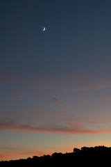 Crescent moon at sunset vertically with varied colors at dusk
