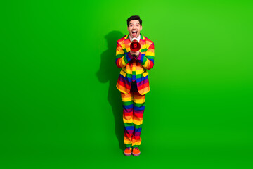 Cheerful man wearing a colorful rainbow suit holding a megaphone against a vibrant green...