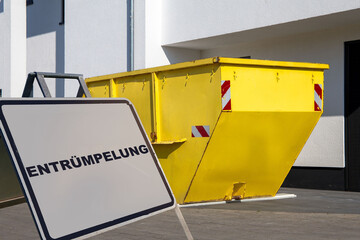 Schild mit der Aufschrift ENTRÜMPELUNG vor einem Absetzcontainer an einem Wohnhaus
