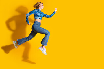 Energetic young woman in a stylish outfit jumping against a vibrant yellow background, expressing...