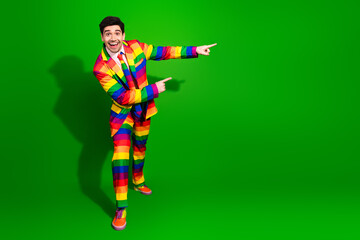 Colorful young man in vibrant rainbow-striped suit posing confidently against a bold green...