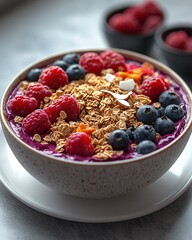 Overhead shot of a brightly colored acai bowl topped with fresh mixed berries, crunchy granola and coconut flakes, beautifully arranged on a white ceramic plate with natural light casting soft shadows