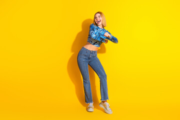 Young cheerful woman in casual outfit dancing joyously on bright yellow background, embodying youthful energy