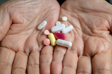 Hand of a senior citizen holding an assortment of real heart-related pills ready for consumption