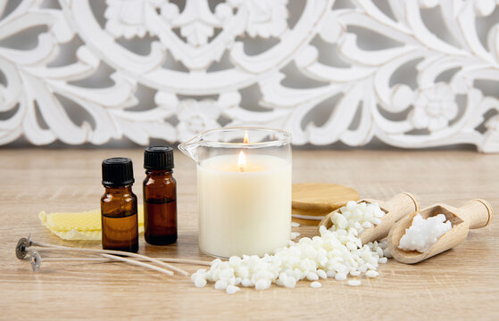 Concept of making scented homemade massage candle. Tools, materials on table fragrance oil bottles, glass jar with pouring spout, coconut wax, soy wax flakes, candle wicks on table. Bohemian style.
