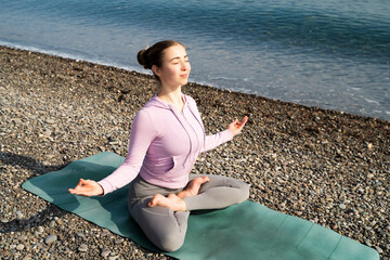 Woman, meditation, pebble sea beach. Peaceful girl in sportswear practices morning yoga sitting in...