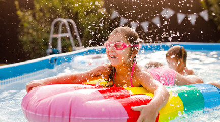 Smiling kid having fun in pool on colorful inflatable toy at summer day
