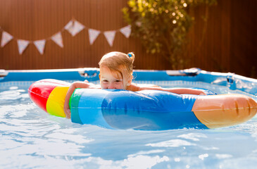 Smiling kid having fun in pool on colorful inflatable toy at summer day