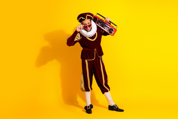 Portrait of a young man in a medieval noble costume with a modern boombox on a bright yellow background, blending past and present styles