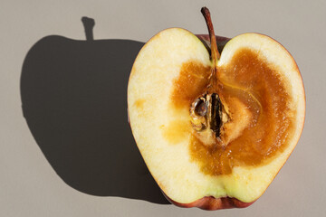 Red apple cut in half with a rotten core and brown spoiled/decayed flesh on a grey background.