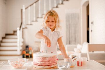 Little girl decorating cake with sprinkles in cozy home kitchen, preparing for birthday party