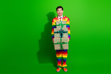 Happy man in colorful rainbow suit holding gifts on green background, celebrating pride, holidays, and diversity with joy and style