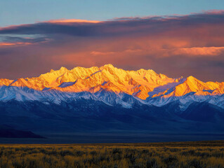 The setting sun's rays are falling on the peak of the distant snow-capped mountains. Beneath the mountains lies a plain. The golden snow-capped peaks and the shadowed slopes and plains below them are 