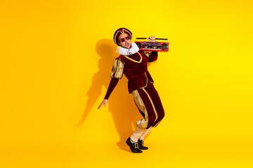 Young man in royal medieval costume holding boombox styled in a retro pose against vibrant yellow...
