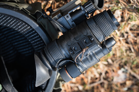 Modern tactical Gen 3 night vision monocular, mounted on a combat helmet, lies on the ground.