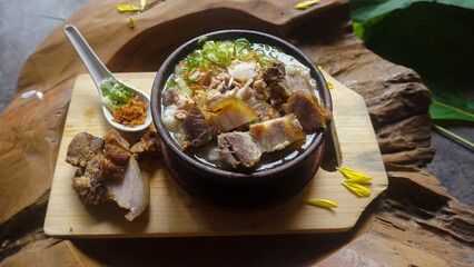 A Bowl of Traditional Pork Porridge with Crispy Toppings and Fresh Scallions, Served on a Wooden Board.