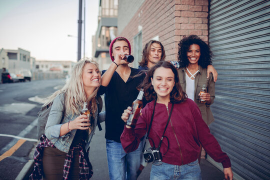 Group of diverse Gen Z friends laughing and walking along urban street at sunset
