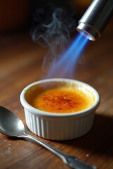 Creme brulee in white ramekin with torch caramelizing sugar on wooden table
