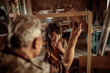 Grandfather teaching grandson woodworking in carpentry workshop