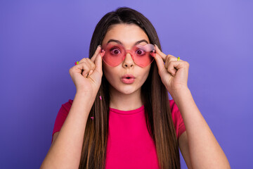 Brunette girl wearing stylish heart-shaped pink sunglass posing playfully against a vibrant purple background