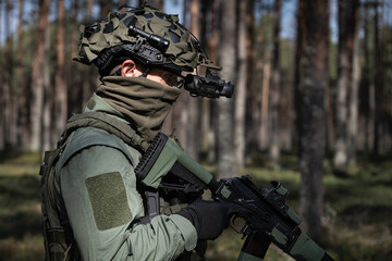 Fototapeta premium Soldier in tactical gear and helmet with NVG in the forest, side view.