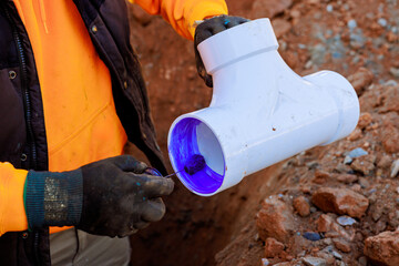 Construction worker is using adhesive on PVC pipe fitting at trench construction site