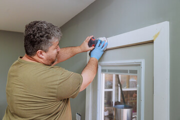 Homeowner works on updating door trim with power sander in well lit interior space during work day.