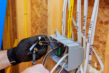An electrician is connecting wires to switch light in junction box while preparing for electrical...