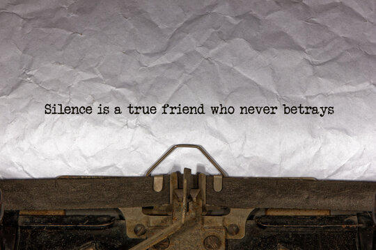 silence is a true friend who never betrays close up of a phrase being typed and centered on a sheet of paper on an old vintage mechanical typewriter.