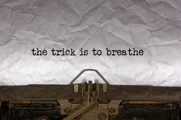 the trick is to breathe close up of a phrase being typed and centered on a sheet of paper on an old vintage mechanical typewriter.