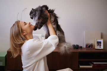 Joyful woman gently lifting fluffy cat capturing playful affectionate interaction indoors...
