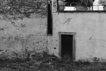 Old stone wall with dark door and plants in a quiet, abandoned space during daylight hours