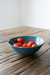 A blue bowl with red tomatoes in it sits on a wooden table
