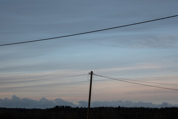 A power line pole is standing in a field with a cloudy sky