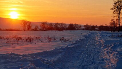 Snowy winter landscape at sunset. Footprints in the snow. Calm, cold mood.