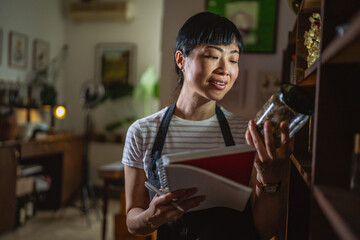 japanese woman artisan write recipes at notebook in herbal workshop